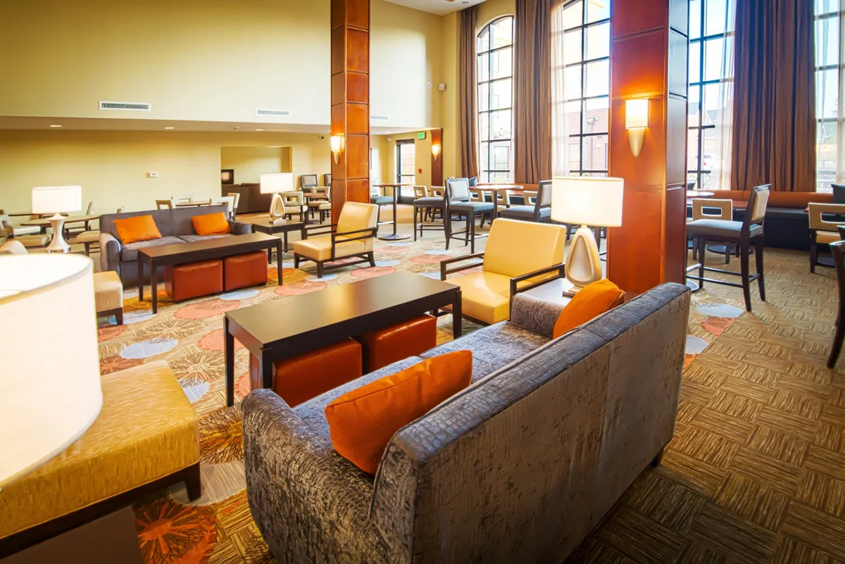 A generously sized living area filled with natural light from large windows, decorated with comfortable seating, a stylish coffee table, and elegant lighting fixtures. The space invites relaxation, socializing, or quiet moments, embodying flexibility and coziness.