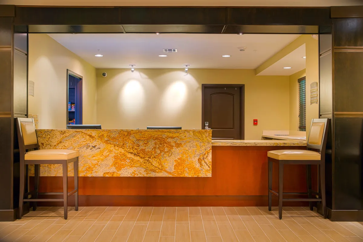 A welcoming lounge and reception area with a granite counter, comfortable seating, and a professional yet inviting atmosphere. Staff members are assisting guests, creating a sense of hospitality and connection.