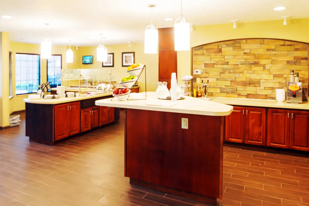 A warm, welcoming dining area centered around a large island countertop adorned with a colorful fruit display. The stone wall and carefully chosen lighting fixtures add character, while the arrangement encourages socializing over meals or morning coffee.