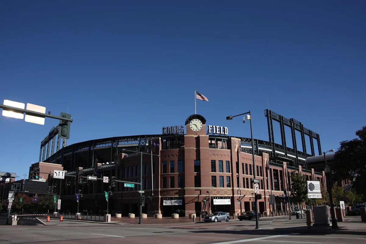 An exterior view of Coors Field, featuring its recognizable sign, a waving flag atop the stadium, and the signature brick facade. The lively energy is palpable, inviting families to imagine themselves attending a baseball game, concert, or community event in the heart of Denver.