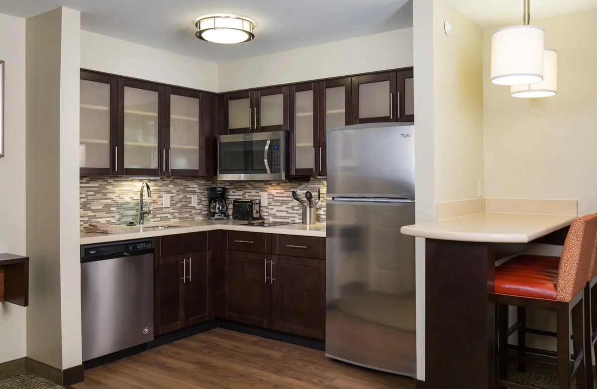 A modern kitchen equipped with dark wood cabinetry, sleek modern appliances, and bar seating. The space is designed for both cooking and entertaining, with functional workspaces and inviting gathering spots.