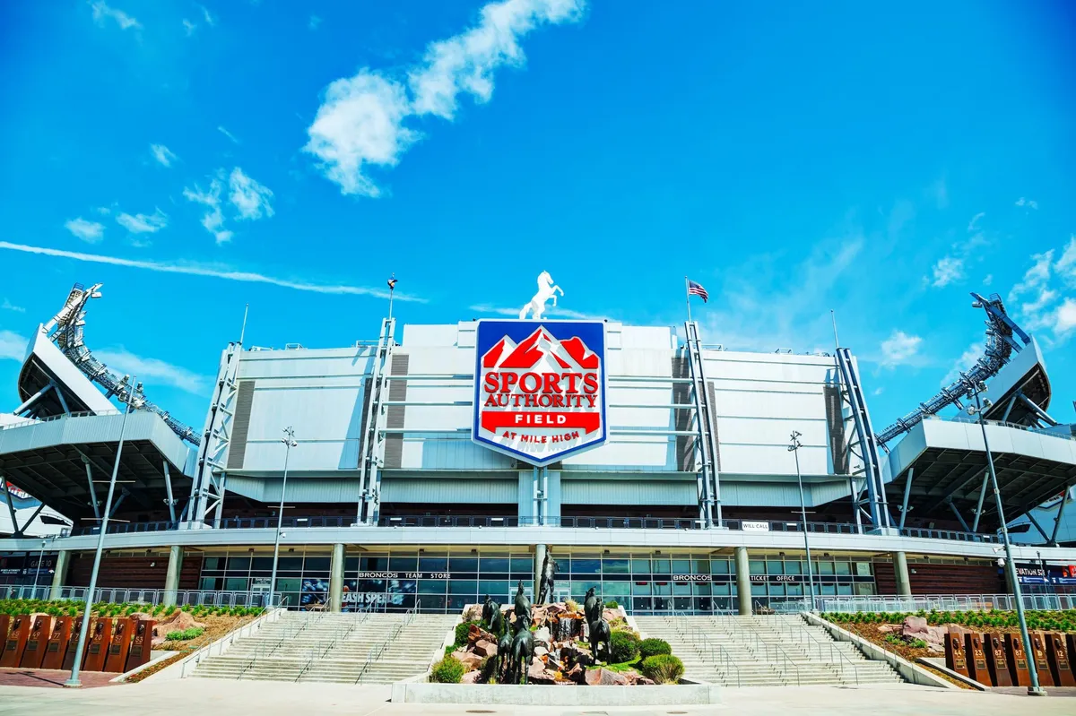 This exterior image features the iconic Sports Authority Field sign, the impressive stadium structure, and lush surrounding landscaping. The scene buzzes with the excitement of sports fans gathered for a major event, suggesting the thrilling atmosphere families can experience when attending a Broncos game or other community gatherings nearby.